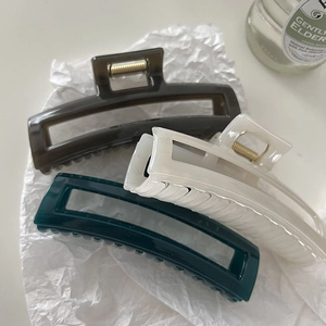 Close-up of matte rectangular hair claws in grey, cream, and green on textured paper