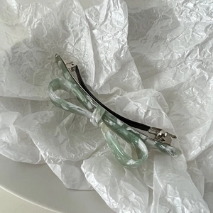 Detailed macro view of green marbled acetate bow hair clip on a white textured background