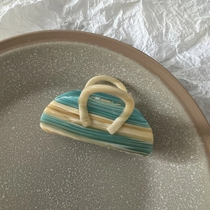 Detail view of large marble texture hair claw clip in blue and cream on ceramic plate