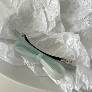 Macro shot of mint green acetate bow hair clip with polished finish on white textured paper