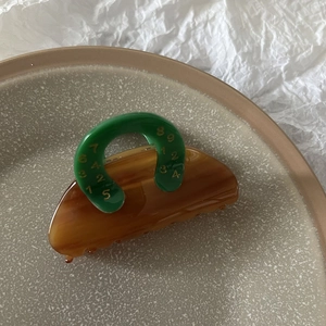 Detailed view of amber claw clip with green U-shaped handle and gold number patterns