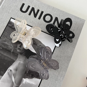 Three butterfly hair claws in beige, black, and transparent grey on a fashion magazine