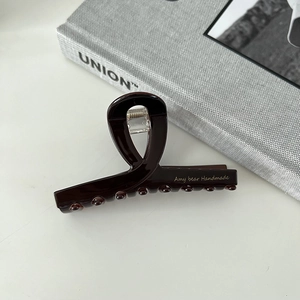 Detailed close-up of dark brown acetate shark clip with elegant gold print on white table