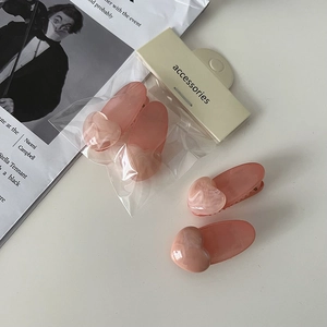 Détail de pinces à cheveux roses avec motifs cœurs en marbre sur fond blanc minimaliste
