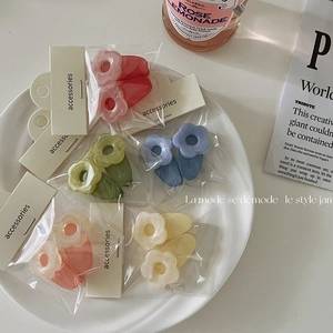 Nahaufnahme bunter Blumen-Haarspangen in Klarsichtverpackung auf einem weißen Teller