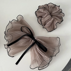Detailed view of taupe pleated organza bow hair clip and matching scrunchie with black edging