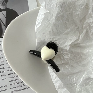 Détail d'une mini pince à cheveux noire avec motif cœur blanc sur une assiette
