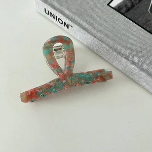 Detail view of acetate hair claw with green and orange marble pattern and metal spring