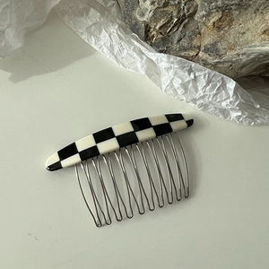 Détail du peigne à cheveux à damier avec dents en métal argenté sur fond de pierre