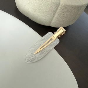 Close-up of duckbill clip with white acetate diamond grid pattern and gold metal finish