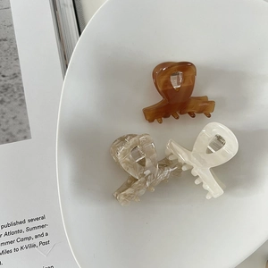 Close-up of three acetate hair clips in tortoise, marble grey, and cream on a ceramic plate