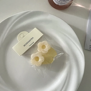 Detail von cremefarbenen Blumen-Haarspangen mit Perlglanz in Verpackung auf weißem Porzellanteller