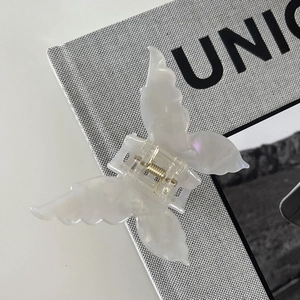 Macro detail of iridescent white butterfly hair claw clip with golden metal spring