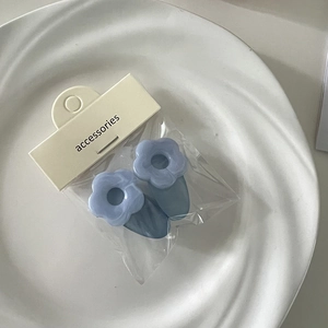 Detailansicht hellblauer matter Blumen-Haarspangen auf weißem Teller mit Verpackung