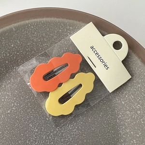 Détail de barrettes à cheveux ondulées en orange et jaune avec emballage d'origine