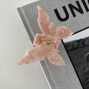 Detail of butterfly hair claw clip with pink marble acetic texture and gold spring