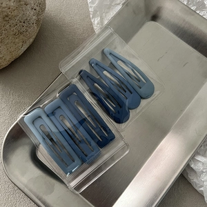 Detail view of matte blue metal hair clips set on a minimalist stainless steel tray