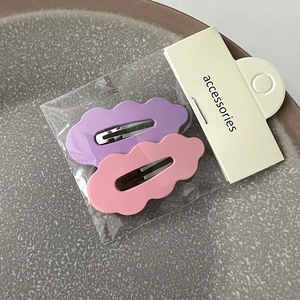 Détail de barrettes à cheveux ondulées violettes et roses présentées dans leur emballage
