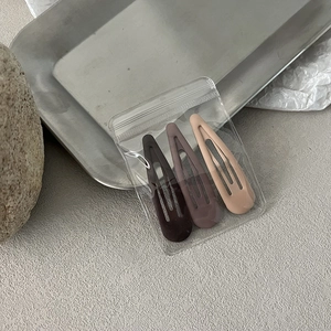 Detailed view of three matte teardrop hair clips in coffee, purple and beige colors