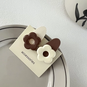 Détail de pinces à cheveux fleurs marron et crème sur un plateau à bijoux en céramique