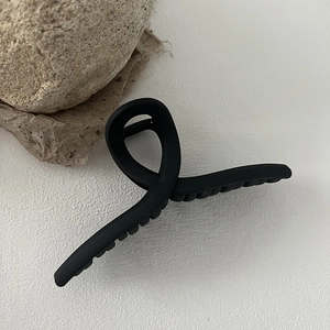 Detail of large matte black cross twist hair claw clip with minimalist finish and texture