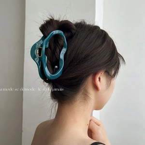 Detail showing an irregular deep green shark hair claw clip in a chic low bun hairstyle