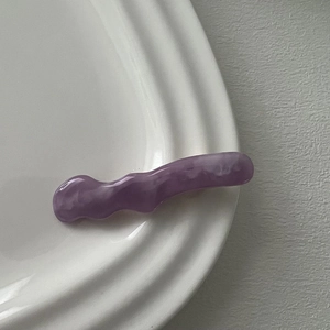 Macro detail of lavender wavy hair clip with marble resin texture on white tray