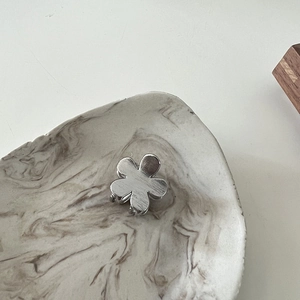 Close-up of a mini silver metal flower hair claw clip with a brushed texture on a marble plate