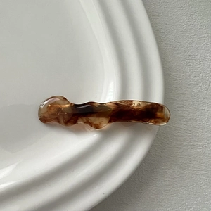 Detail of wave-shaped amber acetate hair clip on a minimalist white ceramic plate