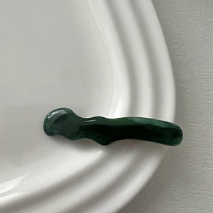 Detailed macro view of dark green wavy resin hair clip with marble texture on ceramic plate