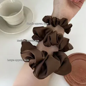 Three sizes of brown satin scrunchies shown on a model's arm for size comparison