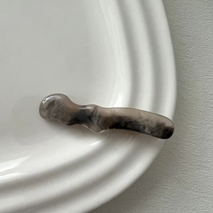 Detail of wavy resin hair clip featuring grey and black marble ink texture on a ceramic dish