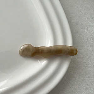 Detail of wavy amber marble resin hair clip placed on white ceramic plate