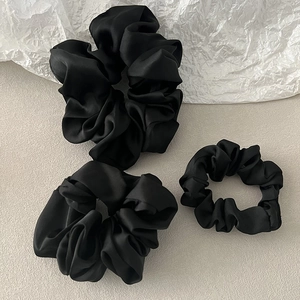 Close-up of three black silky satin hair scrunchies in large and small sizes on sand surface