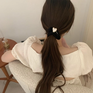 Détail d'un chouchou noir en tissu avec un charme de cœur blanc à bordure dorée