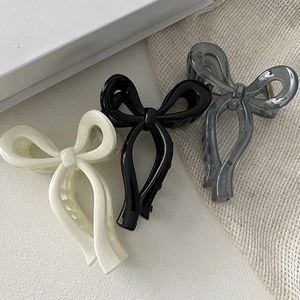 Three bow-shaped hair claw clips in beige, black, and grey, minimalist style set