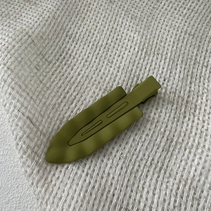 Close-up of olive green matte leaf hair clip with wave texture on natural linen surface