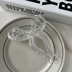 Detail of a transparent ribbon bow hair claw clip showing the inner spring and sleek design