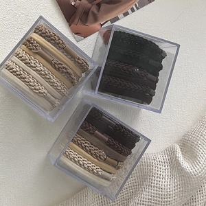 Detail view of woven earth-toned hair ties in a clear acrylic storage box