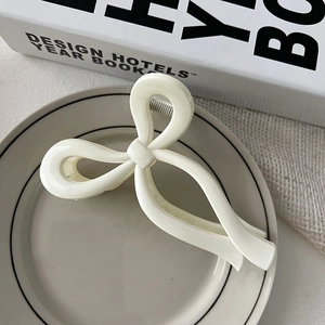 Close-up of a cream-colored ribbon bow hair claw clip displayed on a minimalist plate