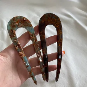 Detail view of two U-shaped resin hair pins with tortoiseshell and marbled textures