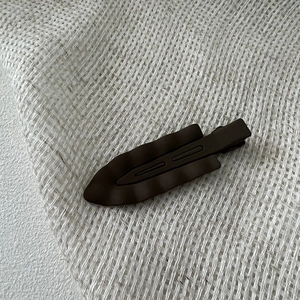 Macro detail of dark coffee matte finish wave hair clip on rustic woven fabric background