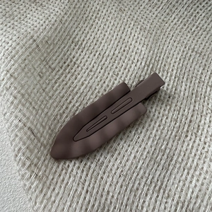 Macro shot of a dark brown matte wavy alligator hair clip on a textured fabric background