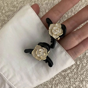 Close-up of black camellia hair clips with pearl detail and golden accents on a sleeve