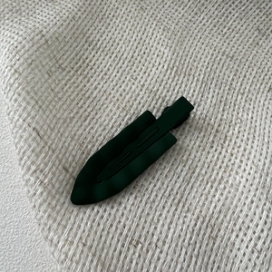 Detailed close-up of dark green matte wavy hair clip on white textured fabric background