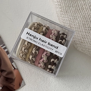 Macro detail of 8-piece braided hair ties set in clear storage box with earthy tones