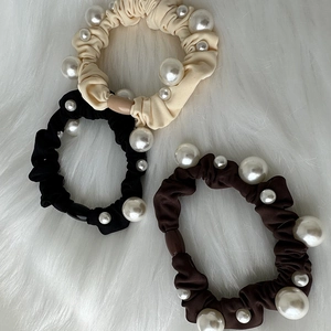 Set of three elegant pleated fabric hair scrunchies with white pearls on plush background