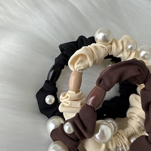 Elegant pearl hair scrunchies in black, beige and brown colors on soft white fur background