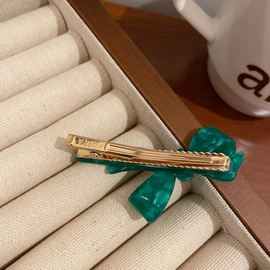 Close-up of emerald green acetate bow hair clip with gold metal base on velvet
