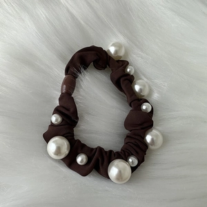 Detailed shot of dark brown fabric scrunchie with white pearl accents on white fur